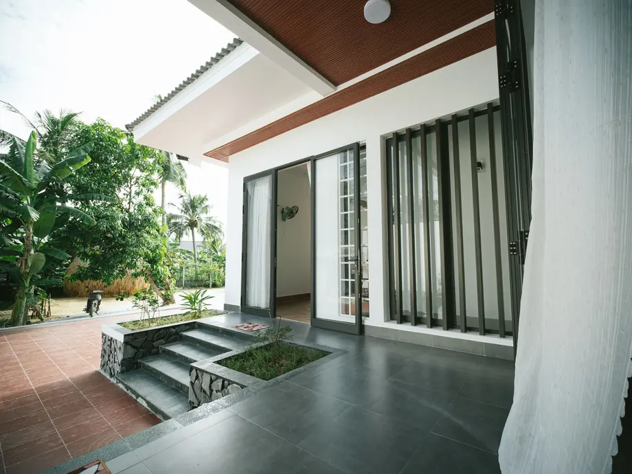 Entrada de una casa residencial en clima tropical, con terraza y palmas al fondo